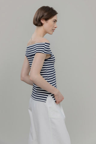 Woman wearing a striped off-shoulder top and white pants against a plain background