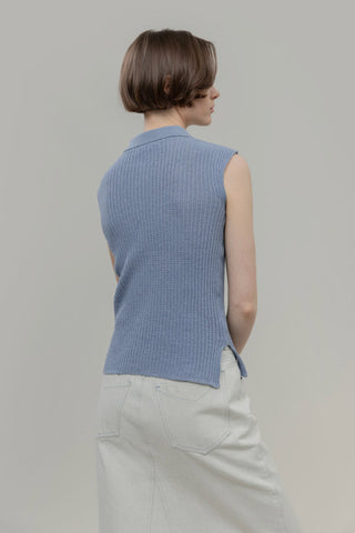 Person wearing a blue sleeveless knitted top against a plain background