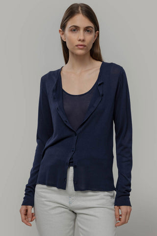 Woman wearing a navy blue cardigan over a navy tank and light gray pants on a gray background