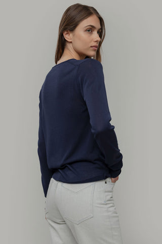 Woman wearing a navy sweater and light gray pants against a plain background