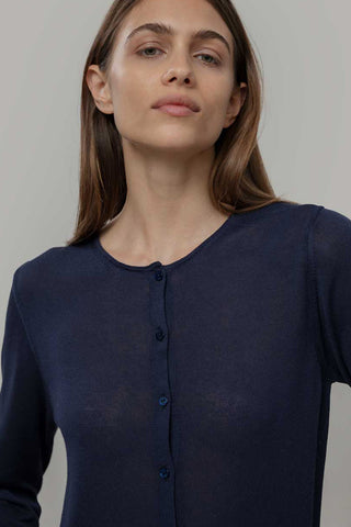 Woman wearing navy blue cardigan in front of grey background. 