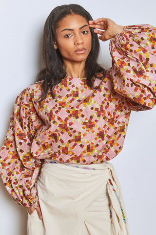 Woman in front of white wall wearing beige wrap bottoms with pink and multi-coloured hand block printed wide sleeve Mira top by Rujuta Sheth. 