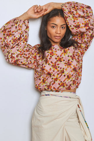 Woman in front of white wall wearing beige wrap bottoms with pink and multi-coloured hand block printed wide sleeve Mira top by Rujuta Sheth. 