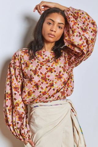 Woman in front of white wall wearing beige wrap bottoms with pink and multi-coloured hand block printed wide sleeve Mira top by Rujuta Sheth. 