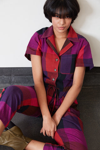 Model sitting on floor wearing jewel tone large Kinetic Check Ray Jumpsuit by Rujuta Sheth. 