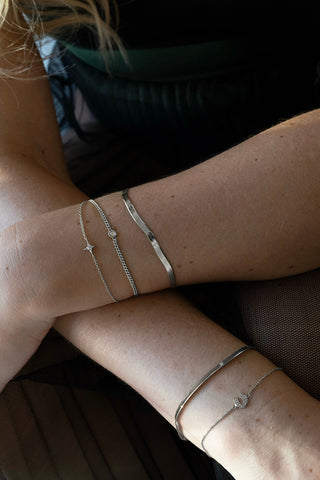 Close-up of woman wearing 3 delicate silver chain bracelets on one arm and 2 on the other. 