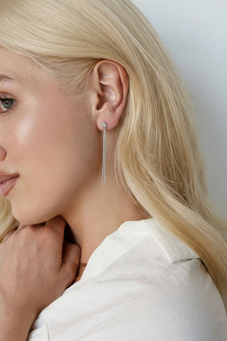 Side profile of woman's face wearing silver chain with opal stone danging earring. 