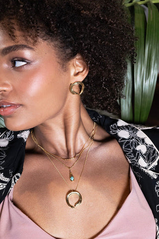 Woman wearing gold hoop earrngs with matching gold chain necklace. 