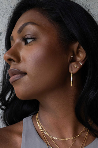 Woman wearing gold earrings and necklaces against a neutral background