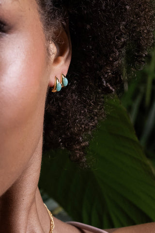 Close-up of a person wearing gold and turquoise earrings with a blurred green background