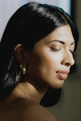 Close-up of woman wearing gold chain necklace and two different sizes of chunky hoop earrings. 
