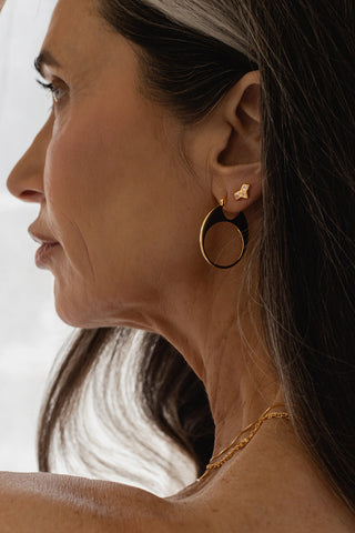 Woman wearing various jewellery, including gold Bae studs by Sarah Mulder. 