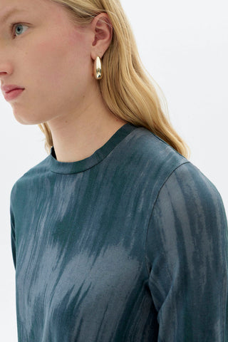 Close-up of woman in front of white background wearing blue organic cotton ombre print Brisa long sleeve top by Thinking Mu. 