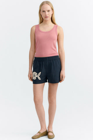Woman wearing pink tank top and black shorts with lace fish appliqué. 