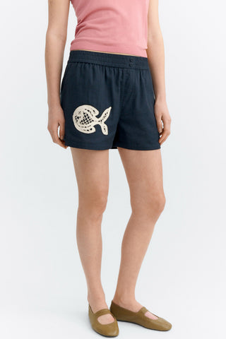 Woman wearing pink tank top and black shorts with lace fish appliqué. 