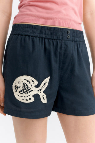 Close-up of woman wearing pink tank top and black shorts with lace fish appliqué. 