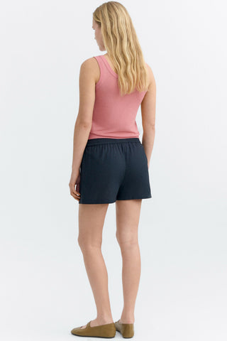 Back view of woman wearing pink tank top and black shorts with lace fish appliqué. 
