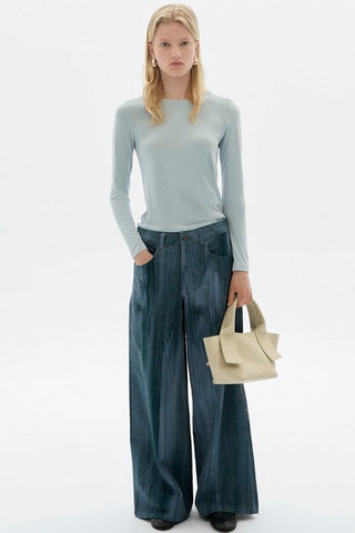 Woman in front of white background wearing light blue long sleeve top and wide leg Heda jeans by Thinking Mu. 