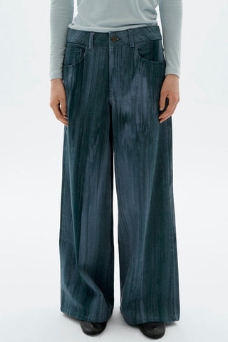 Close-up of woman in front of white background wearing light blue long sleeve top and wide leg Heda jeans by Thinking Mu. 