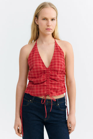 Woman wearing red checkered halter neck top with ruching detail on front and navy jeans. 