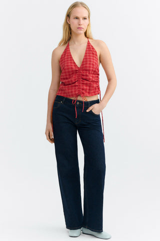 Woman wearing red checkered halter neck top with ruching detail on front with dark denim jeans. 