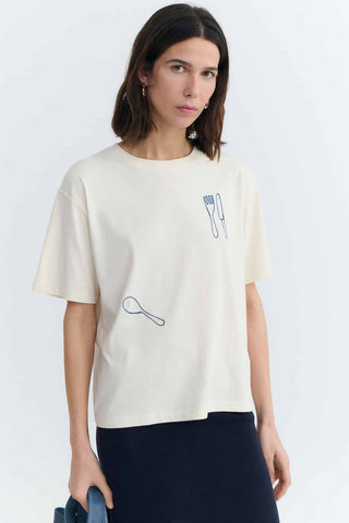 Woman wearing white t-shirt with blue cutlery embroidery. 