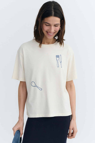 Woman wearing white t-shirt with blue cutlery embroidery. 