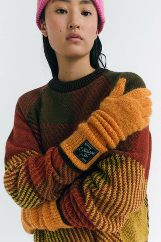 Close-up of model wearing multicolour sweater and orange Maggie gloves by Thinking Mu. 