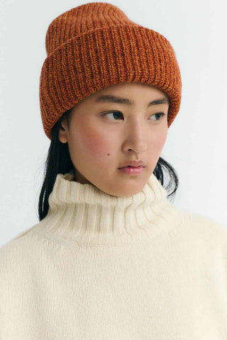 Woman wearing a cream high neck sweater and orange thick knit wool Ruby Beanie by Thin king Mu.