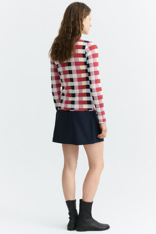A woman shown from the back wearing a red, white, and black check long-sleeve top, a dark black mini skirt, and black ankle boots, against a plain white studio background.