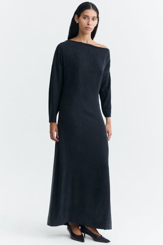 A woman modeling a long, off-the-shoulder black full length dress with long sleeves, photographed against a clean white studio background.