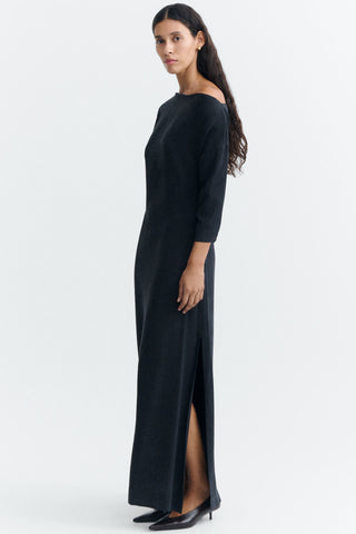 A woman modeling a long, off-the-shoulder black full length dress with long sleeves, photographed against a clean white studio background.