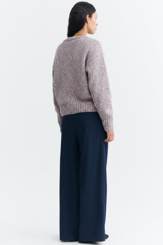 A woman shown from the back wearing a multicolor knit sweater and dark navy wide-leg trousers, standing against a plain white studio background.
