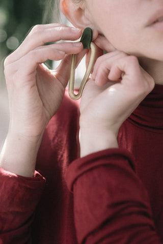 Woman putting on green and brass earring. 