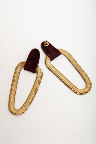 A pair of earrings featuring textured gold snake-chain loops connected to burgundy suede tabs with gold studs, displayed on a clean white background.