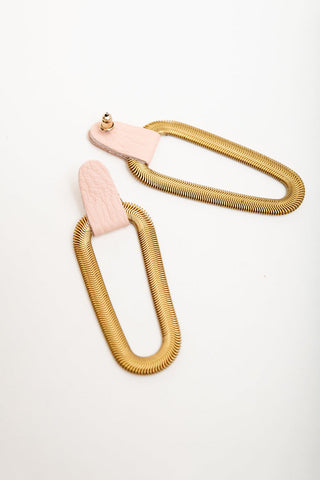 A pair of earrings featuring textured gold snake-chain loops connected to light pink leather tabs with gold studs, displayed on a clean white background.