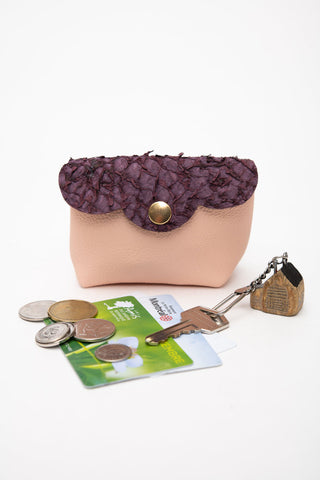 Small pink leather coin purse with purple  scalloped flap, shown on white background with keychain & key, metro cards and coins. 