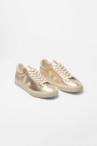 A pair of metallic rose gold sneakers with cream-colored laces and soles, displayed on a clean white studio background.