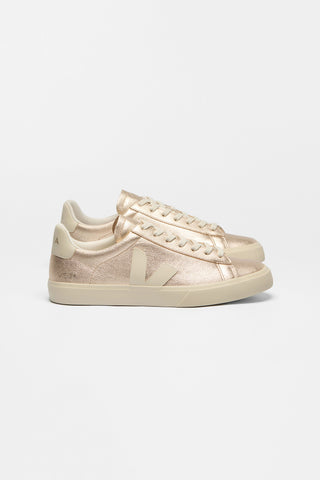A pair of low-top sneakers in a metallic rose gold leather with Veja V logo in cream, shown from the side against a plain white background. 