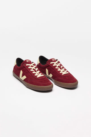A pair of dark red suede sneakers with cream-colored laces and a cream Veja 'V' logo, set against a plain white background.
