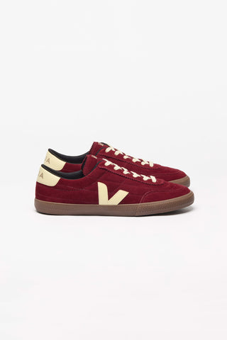 A pair of dark red suede sneakers with cream-colored laces and a cream Veja 'V' logo, set against a plain white background.