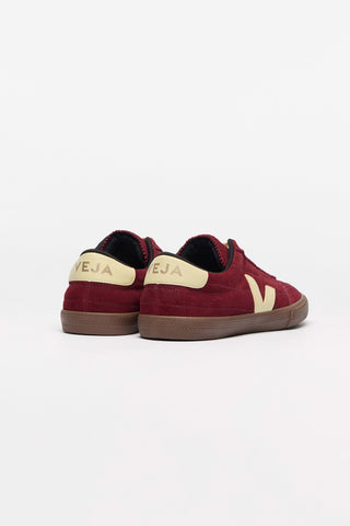 A pair of dark red suede sneakers with cream-colored Veja 'V' logo, shown from the back set against a plain white background.