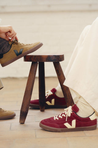 Knee down photo of two people wearing Veja sneakers, one camel coloured suede, the other burgundy coloured suede. 