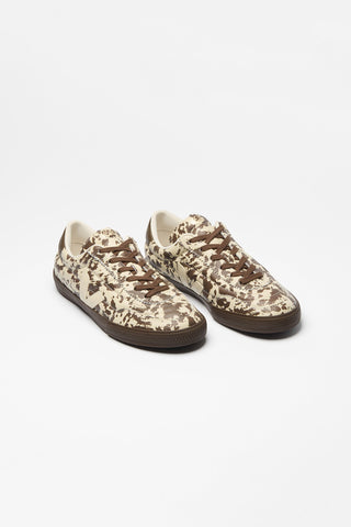 A pair of biege low-top sneakers with brown cowhide print, brown laces and cream Veja V logo, photographed on a clean white background.