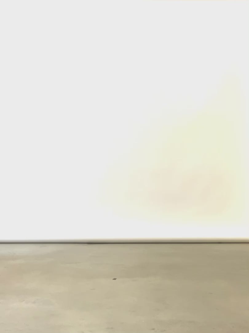 A woman walks across the screen in a neutral studio, wearing a white long sleeve blouse and black drawstring waist pants paired with black heeled boots. 