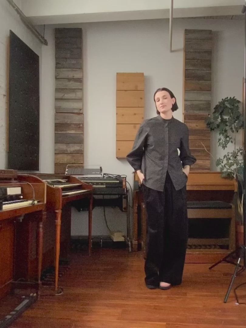 Video of woman in recording studio with pianos in the background, wearing black star print button up Dahlia shirt and black wide leg Zorah pants, both by Jennifer Glasgow. 