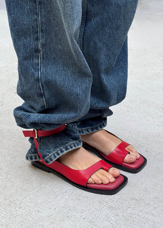 Red sandals worn with blue jeans on a light gray background