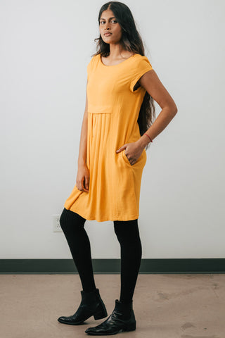 Model wearing Jennifer Glasgow Saiwa pleated dress in yellow OEKO-TEK linen blend.