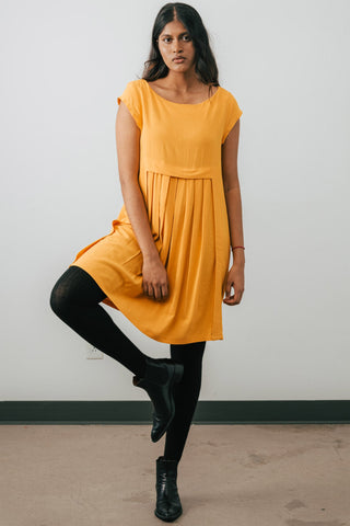 Model wearing Jennifer Glasgow Saiwa pleated dress in yellow OEKO-TEK linen blend.