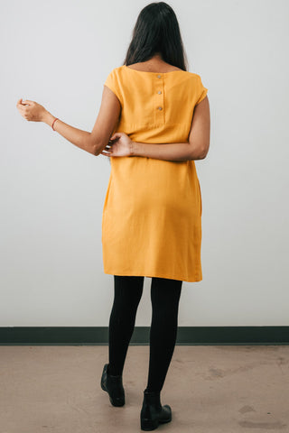 Back view of model wearing Jennifer Glasgow Saiwa pleated dress in yellow OEKO-TEK linen blend.
